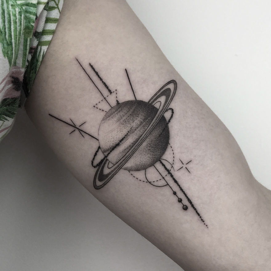 Geometric tattoo design of Saturn with lines and dots on an arm.