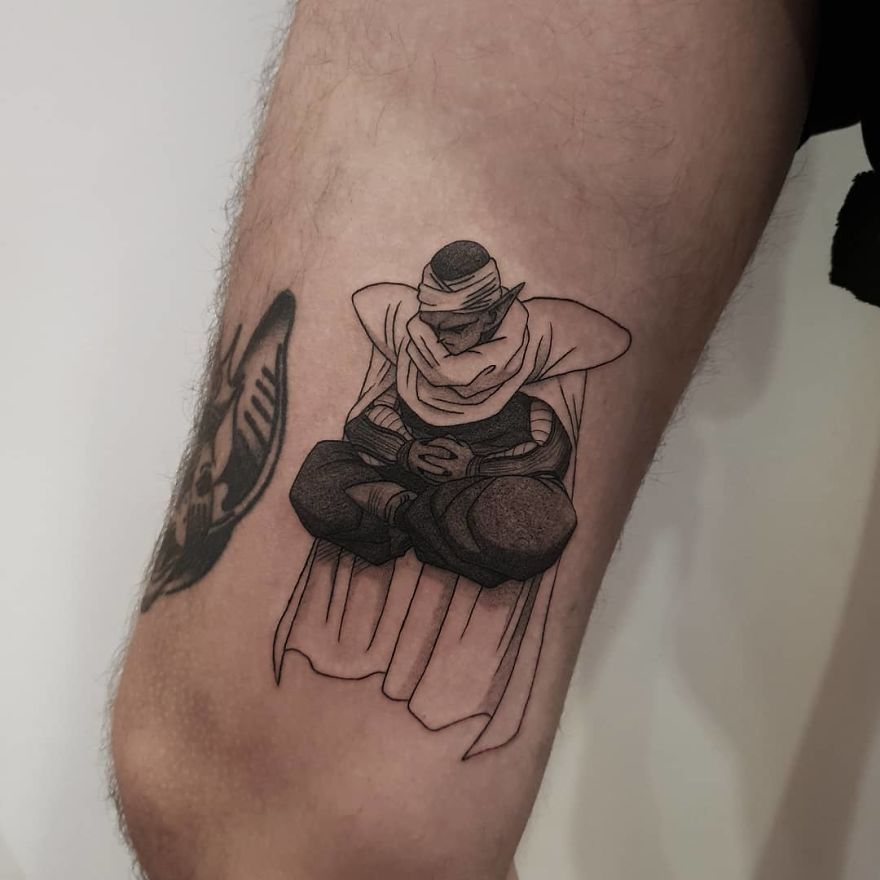 Dragon Ball tattoo on a person's leg depicting a character Piccolo in a meditative pose, showcasing detailed shading and line work.
