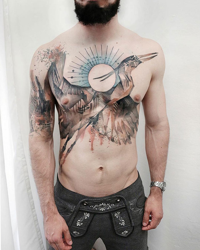 Man displaying incredible chest tattoo featuring a bird design with artistic elements.