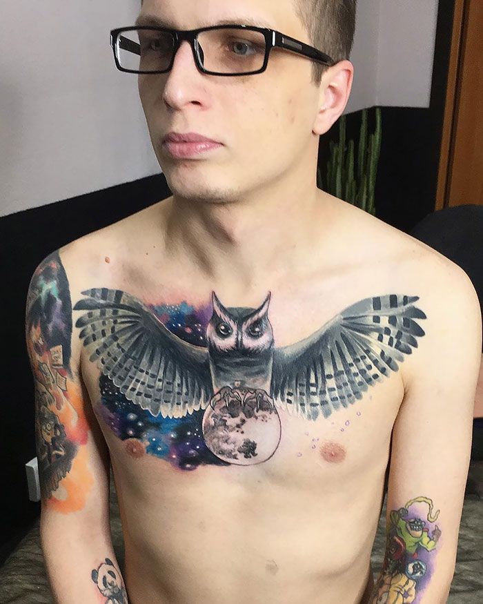 Man with an incredible chest tattoo of an owl holding a moon, showcasing colorful ink.