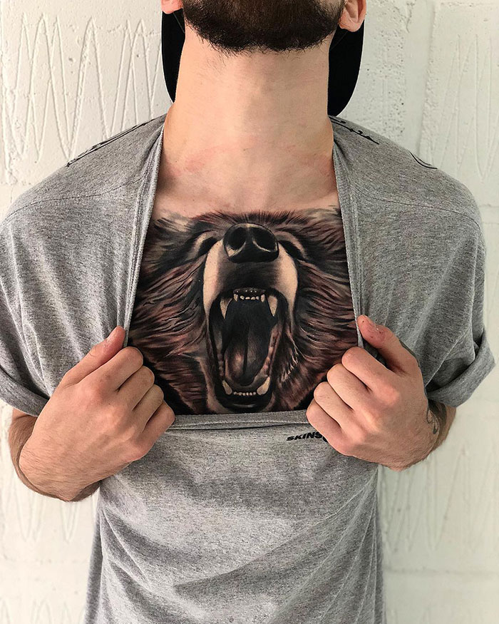 Man revealing a detailed roaring bear chest tattoo under a gray shirt.