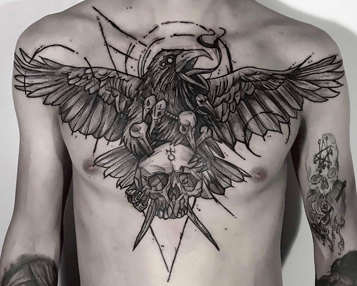 Chest tattoo featuring a detailed raven and skull design in black and gray.