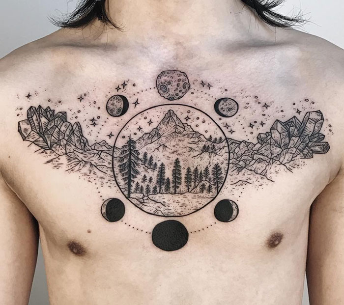 Chest tattoo featuring a mountain landscape with moon phases and crystals.