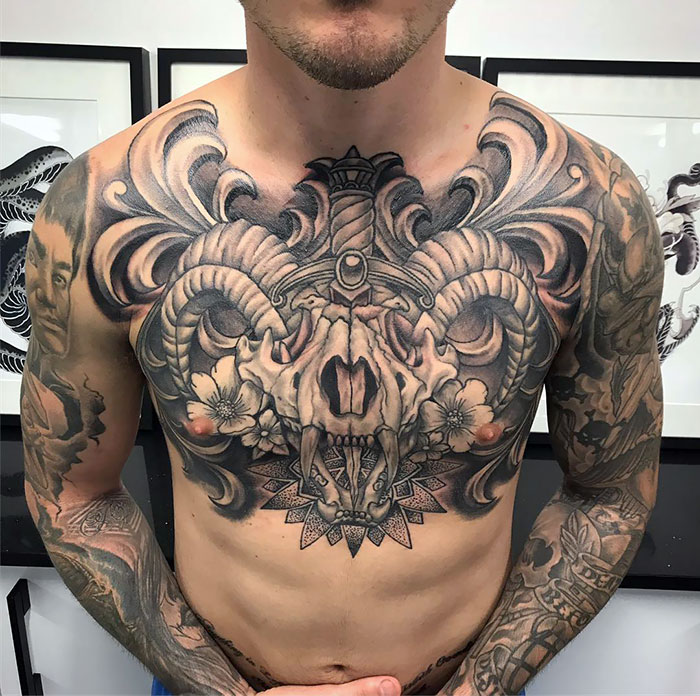 Detailed chest tattoo featuring intricate designs and floral patterns on a man's torso.