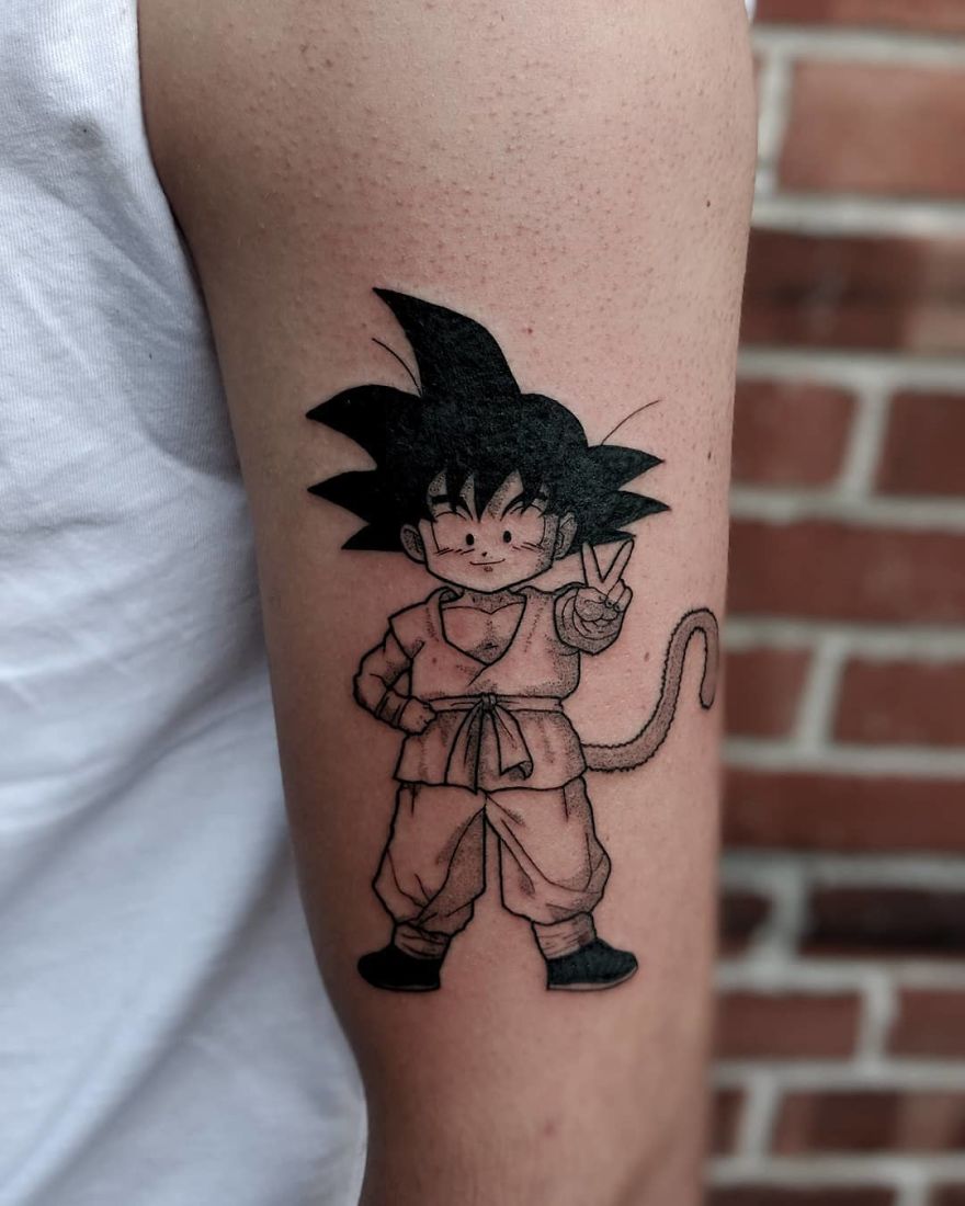 Dragon Ball tattoo of Goku on an arm, illustrating anime character in black ink against a brick background.