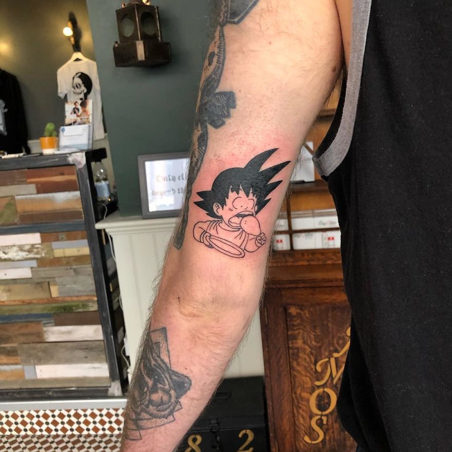 Dragon Ball tattoo of Goku eating on a person's forearm in a tattoo studio.
