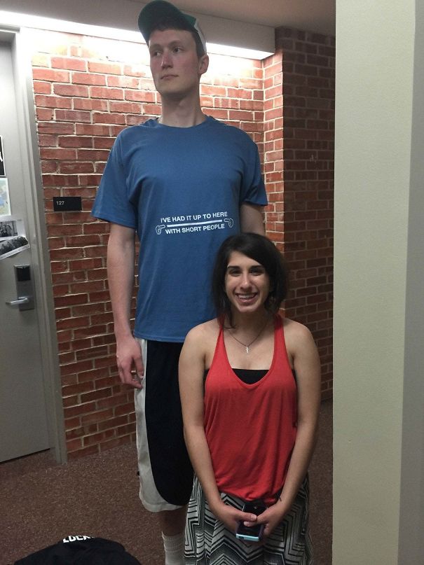 Tall man in a blue shirt standing behind a shorter woman smiling, highlighting everyday struggles of tall people.