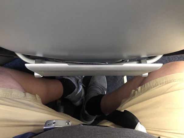 Person with long legs cramped in a small airplane seat, illustrating common struggles of tall people in everyday situations.