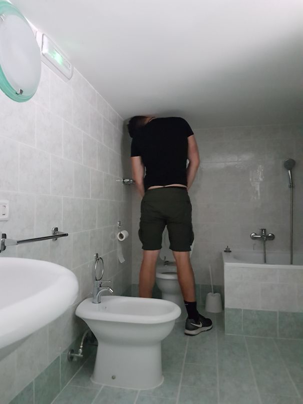 Tall man struggling to stand in a low-ceiling bathroom, highlighting everyday struggles of tall people.