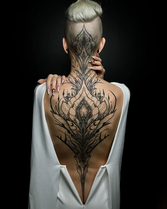 Intricate back tattoo masterpiece on a person with a shaved head, wearing a white open-back garment.