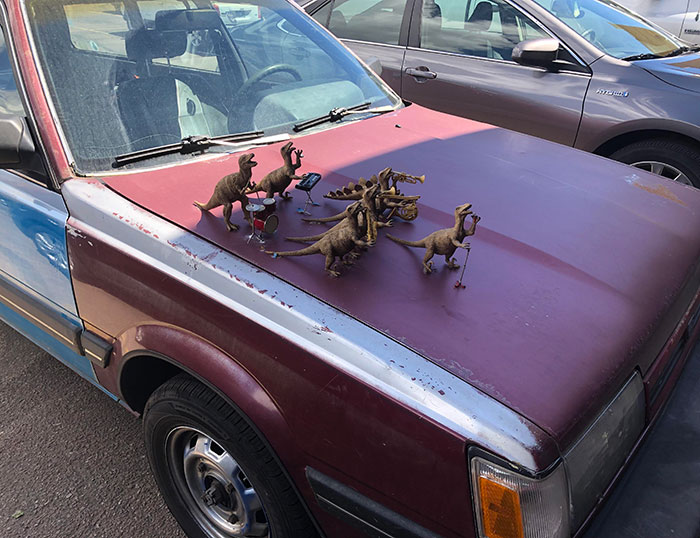 Funny car with toy dinosaur band on hood, parked on the street.