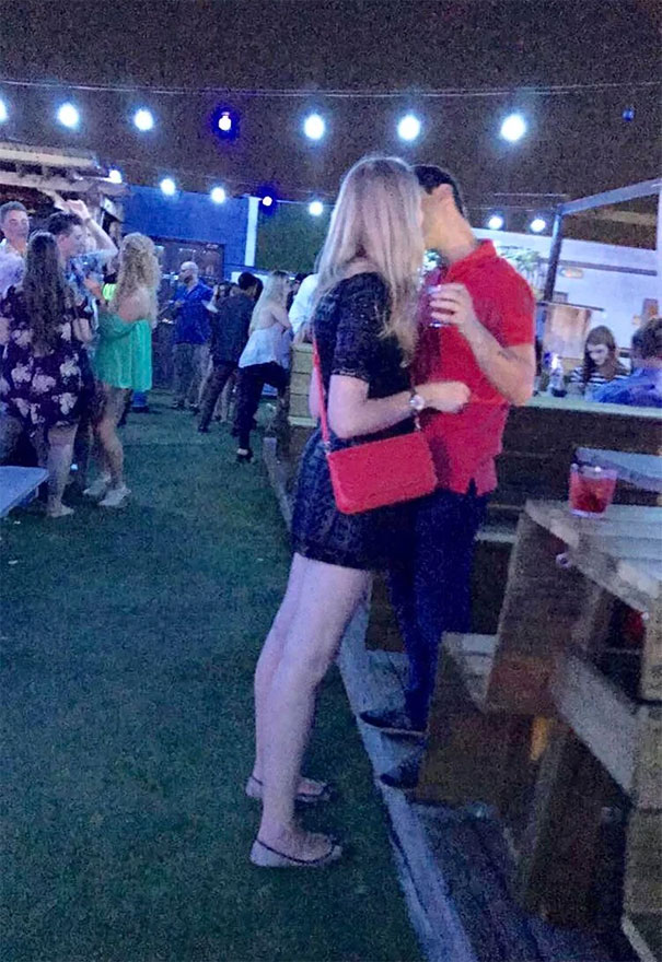 Tall woman leaning down to kiss shorter man at an outdoor nighttime party, illustrating tall people everyday struggles.