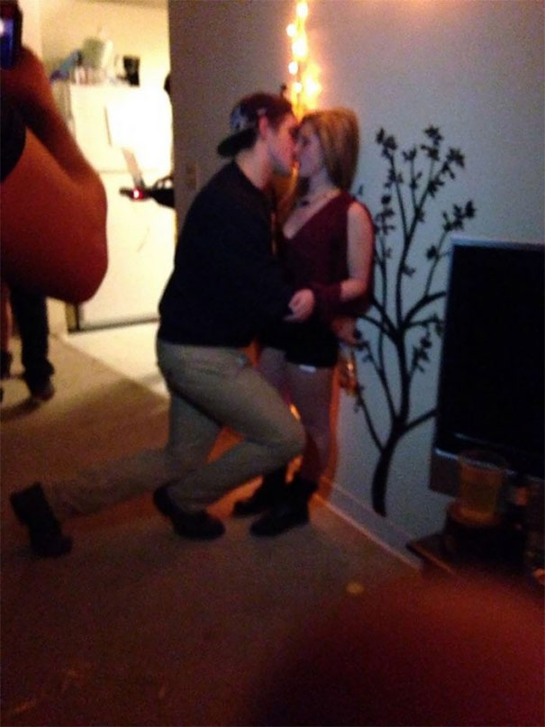 A tall person kneeling to kiss a shorter person against a wall, highlighting everyday struggles of tall people.