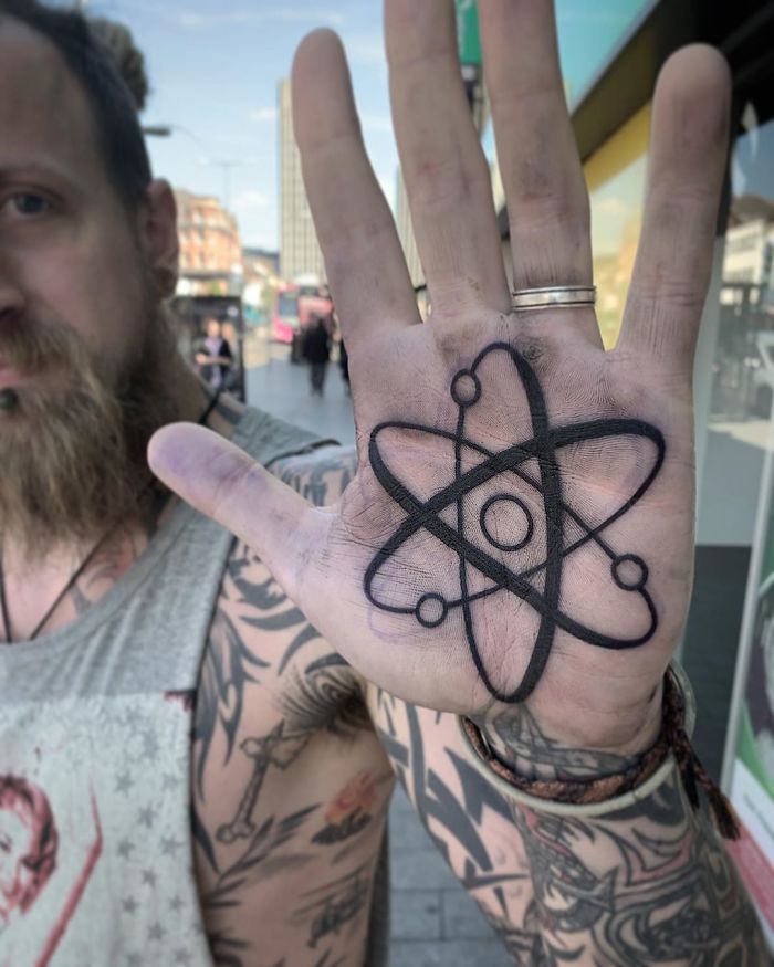 Man displaying palm tattoo featuring an atomic design, showcasing one of the best palm tattoos in an urban setting.