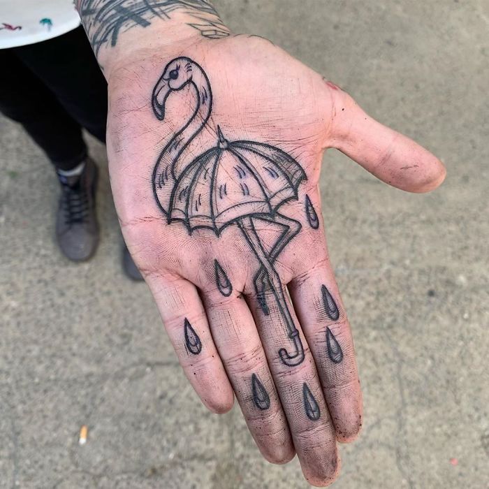 Close-up of a palm tattoo featuring a flamingo and umbrella design, complete with raindrop details.