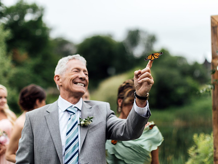 Older man at wedding smiling with a butterfly landing on his hand during a family tribute honoring groom’s sister. Older man at wedding smiling with a butterfly landing on his hand during a family tribute honoring groom’s sister.