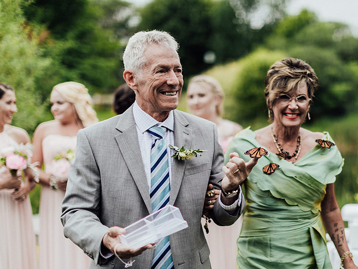 Groom's family releases butterflies during wedding, one butterfly lands gently on the father's hand in outdoor ceremony. Groom's family releases butterflies during wedding, one butterfly lands gently on the father's hand in outdoor ceremony.