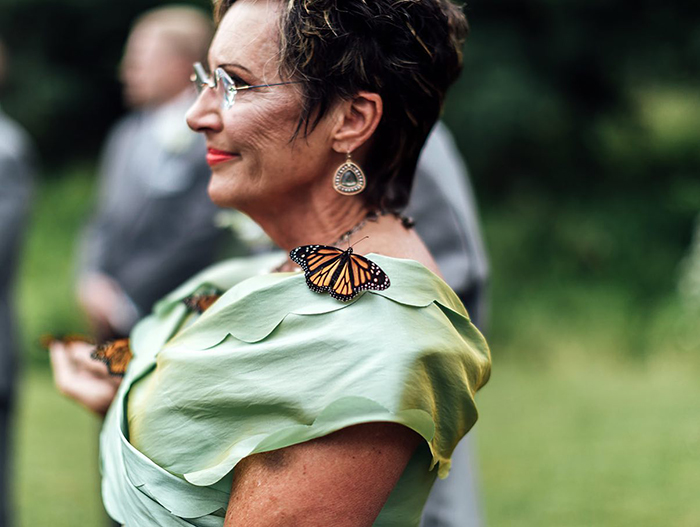 Woman at wedding with butterfly on her shoulder during groom's family butterfly release honoring his sister who died Woman at wedding with butterfly on her shoulder during groom's family butterfly release honoring his sister who died
