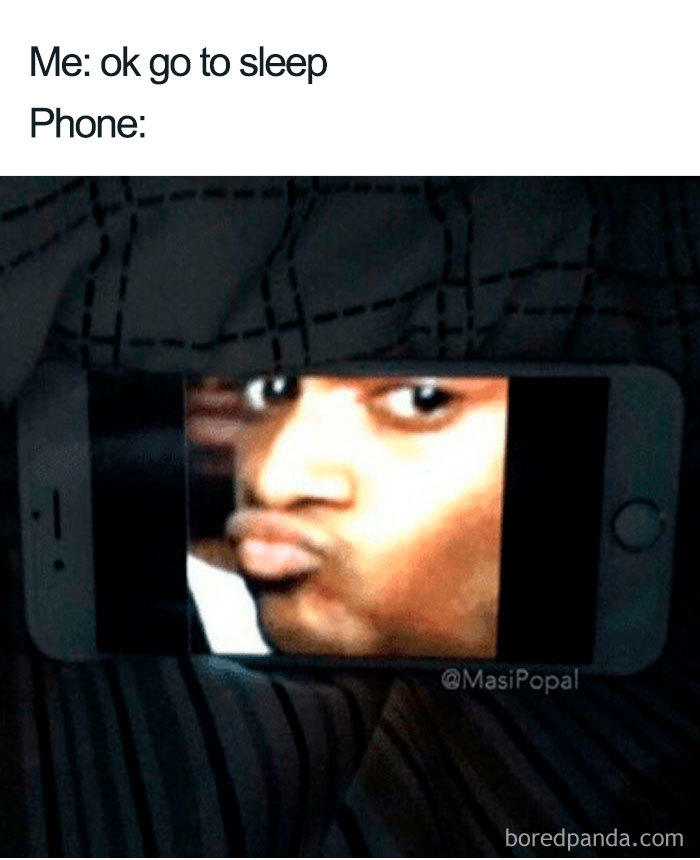 Phone screen under blanket showing a funny face meme, illustrating the struggle of sleeping with distractions in sleeping memes.