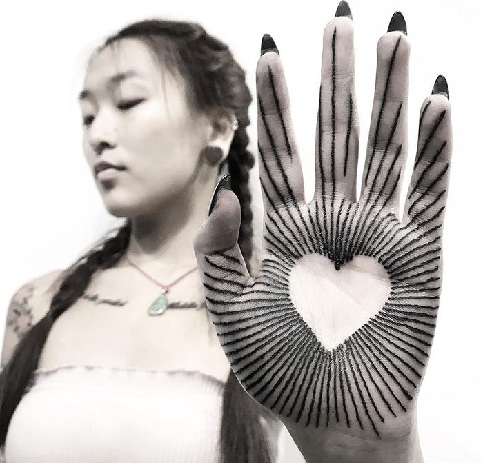 Woman displaying a palm tattoo with a heart and radiating lines.