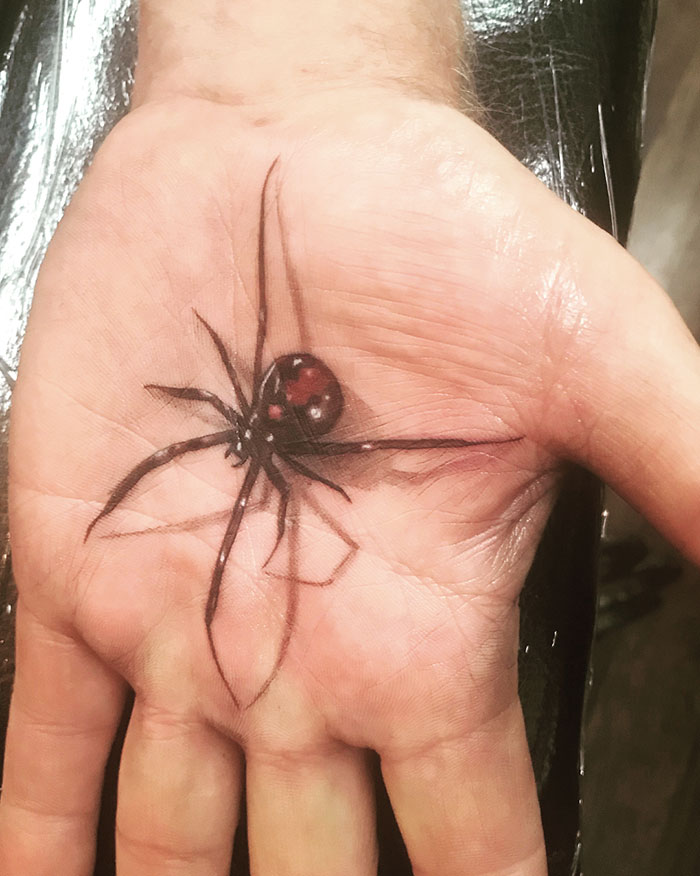Realistic spider palm tattoo with intricate details on a person's hand.
