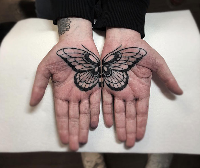 Butterfly design tattooed on both palms, showcasing intricate lines and symmetry.