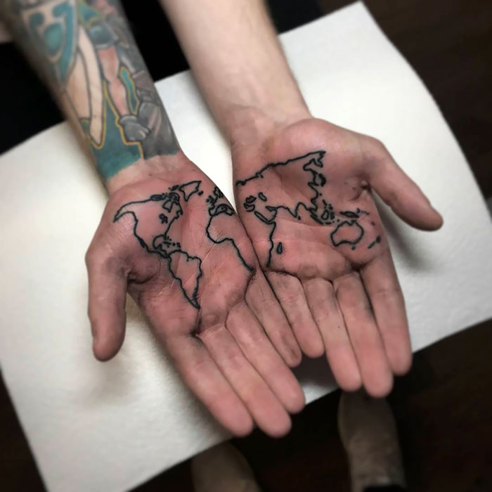 Palm tattoos of a world map on two hands, displaying continent outlines in black ink.