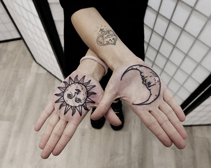 Sun and moon designs inked on palms, showcasing detailed palm tattoos in a minimalist setting.