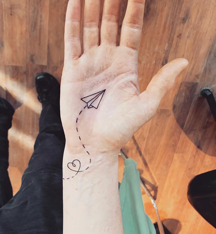 Hand with a minimalist palm tattoo of a paper airplane and heart, showcasing one of the best palm tattoos.