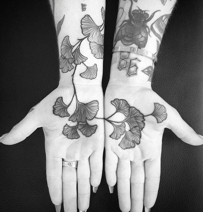 Intricate palm tattoos of ginkgo leaves on both hands, showcasing detailed black ink artistry.
