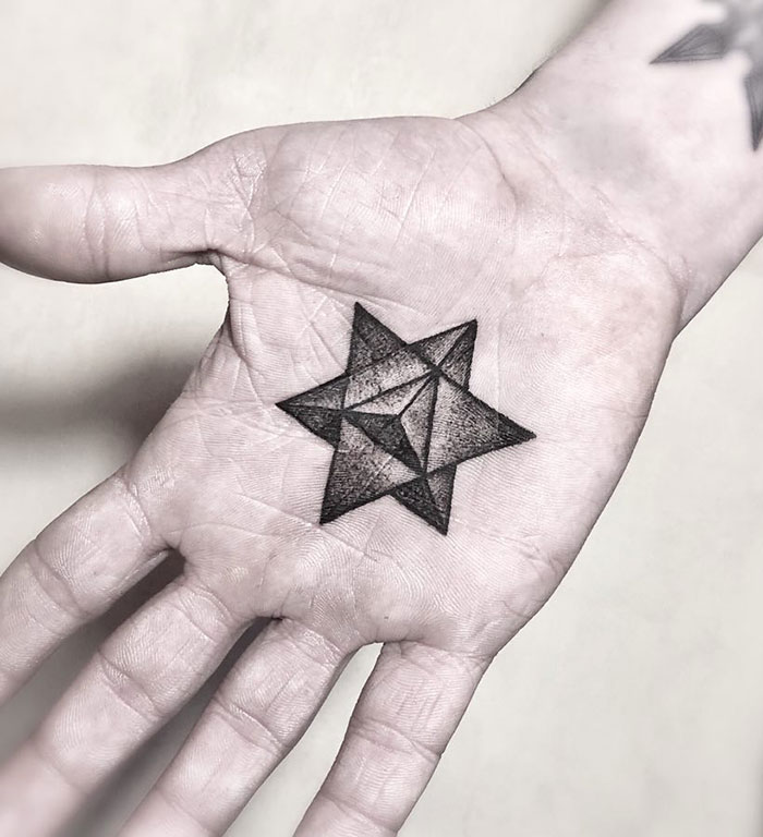 Geometric star design palm tattoo on an open hand, showcasing intricate black ink details.