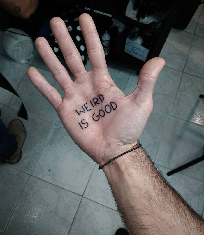 A palm tattoo reading "WEIRD IS GOOD" on an open hand, highlighting creative palm designs.