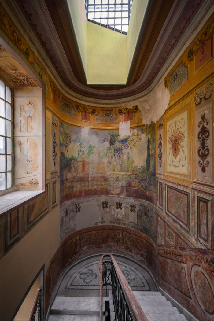 Ornate painted walls and skylight inside an abandoned place in Tbilisi with a curved staircase.