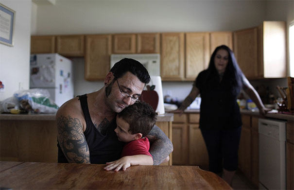 Man with tattoos embraces child at kitchen table, symbolizing transformation and family values. Man with tattoos embraces child at kitchen table, symbolizing transformation and family values.