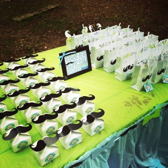 Party favor boxes with mustache decorations displayed on a green table, reflecting trends from the past decade.
