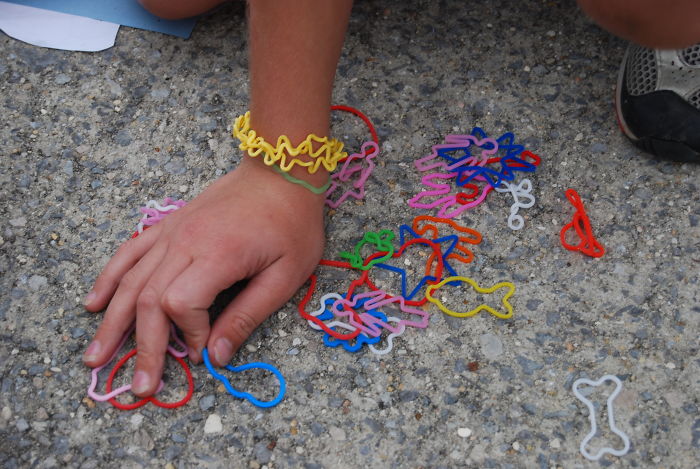 Child's hand playing with colorful forgotten trends rubber band shapes on rough concrete ground, representing hottest trends.