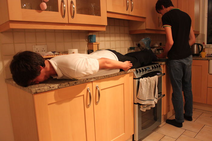 Two young men in a kitchen with one lying face down on the counter depicting forgotten hottest trends from the past decade.