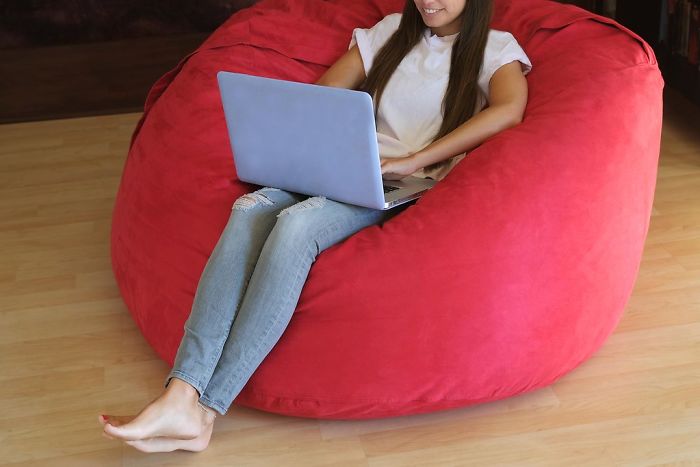Woman sitting on a large red bean bag using a laptop, representing popular trends from the past decade forgotten by many.