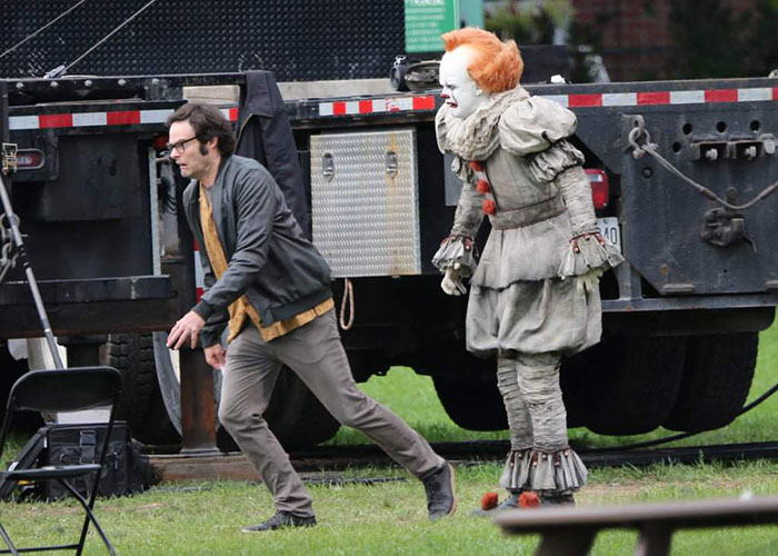 Bill Hader reacting on set as Pennywise, with crossed eyes, follows behind in costume near a truck.