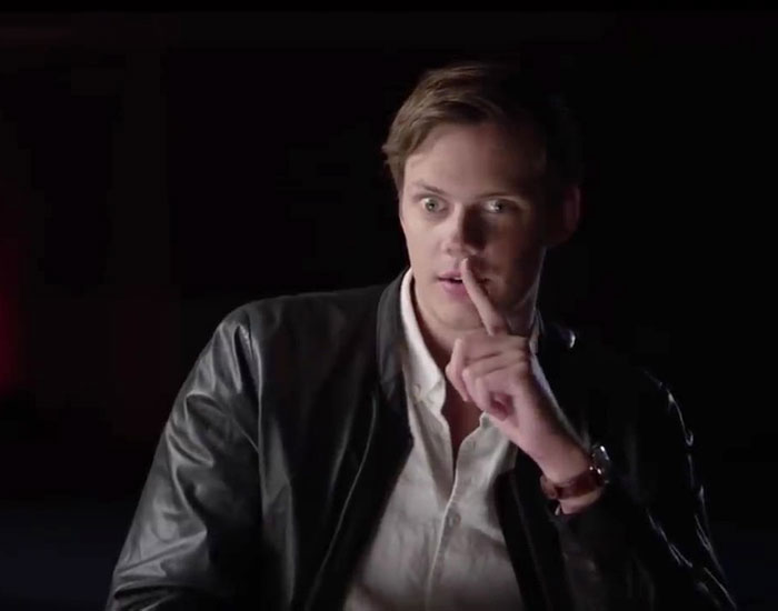 Actor demonstrating crossed eyes like Pennywise, wearing a leather jacket and pointing to his lips, in a dark setting. Actor demonstrating crossed eyes like Pennywise, wearing a leather jacket and pointing to his lips, in a dark setting.