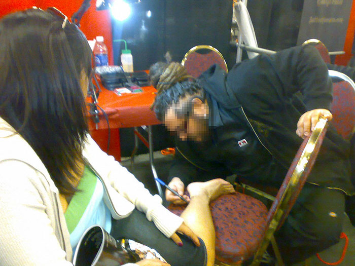Artist applies a tiny but costly tattoo on woman's leg during an event.