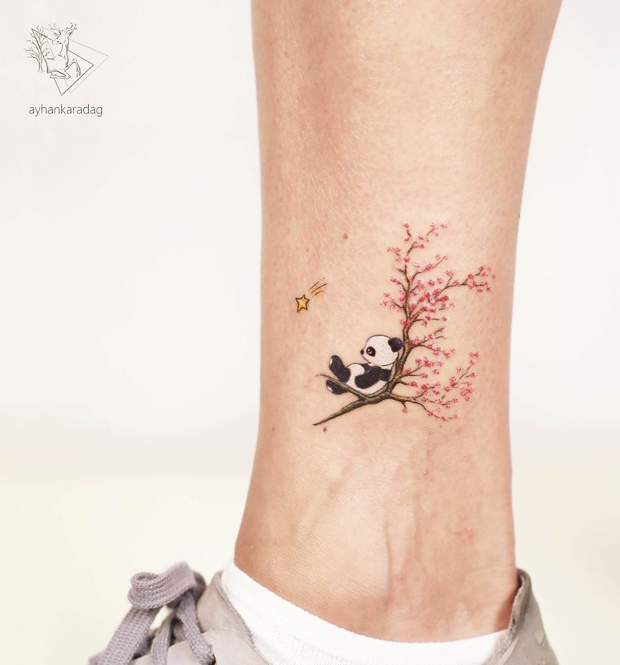 Panda tattoo design on ankle with pink cherry blossom branch and small star.