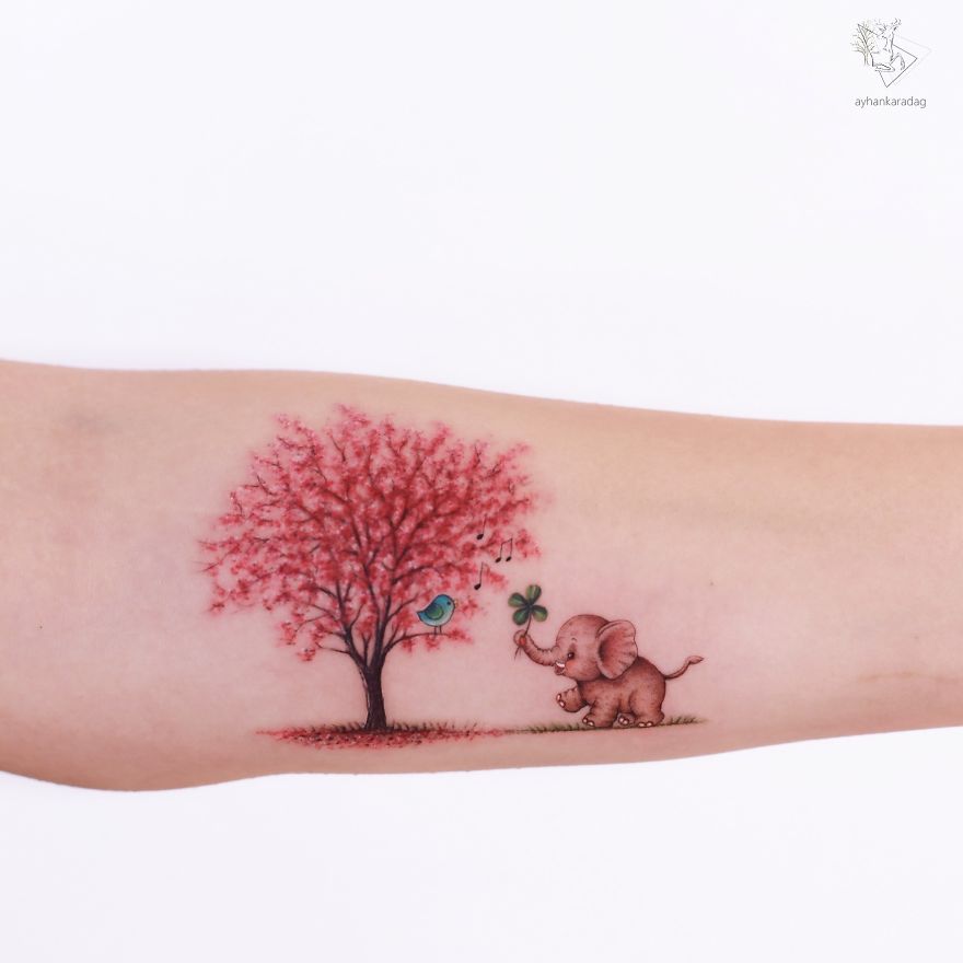 Tattoo design featuring an elephant with a clover, a vibrant tree, and a bluebird on human skin.