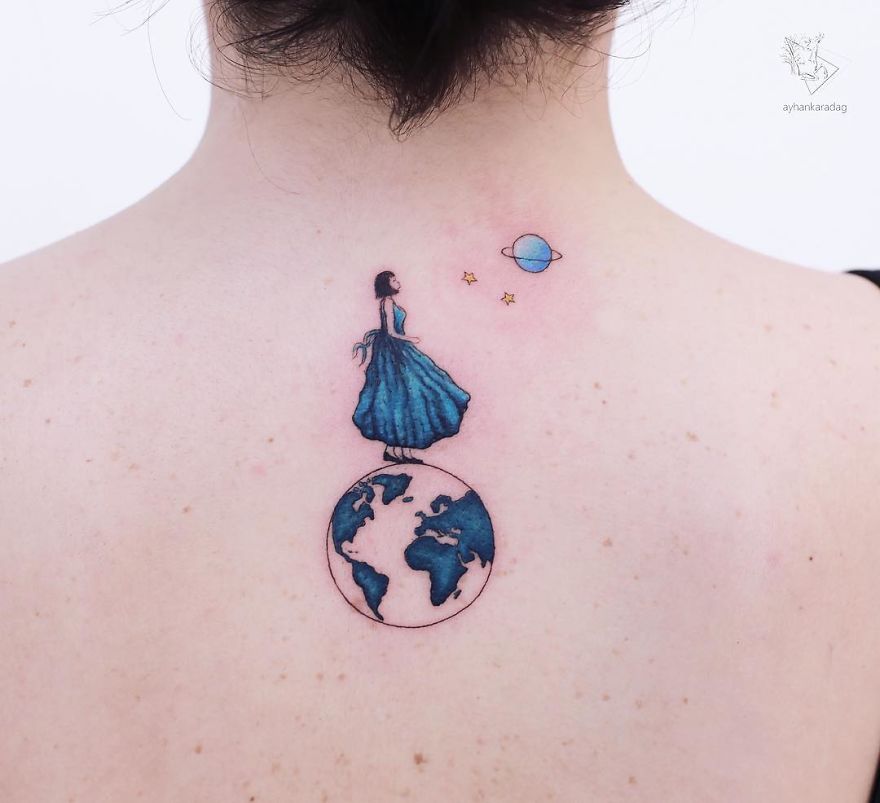 Tattoo design of a woman in a blue dress standing on Earth with a planet and stars, inked on human skin.