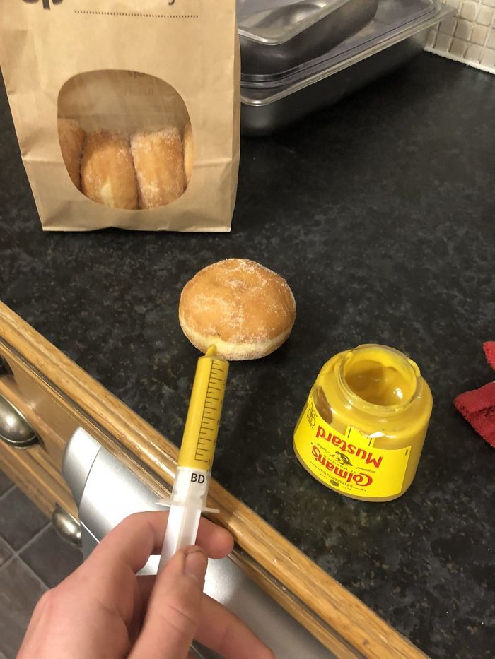 Person infusing a donuts with mustard 