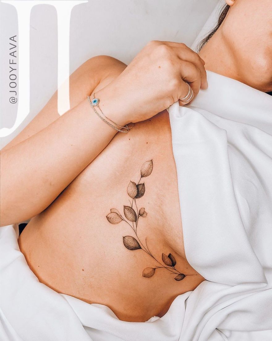 Delicate feminine tattoo of leaves on a woman's side, wrapped in white fabric, showcasing elegant design.