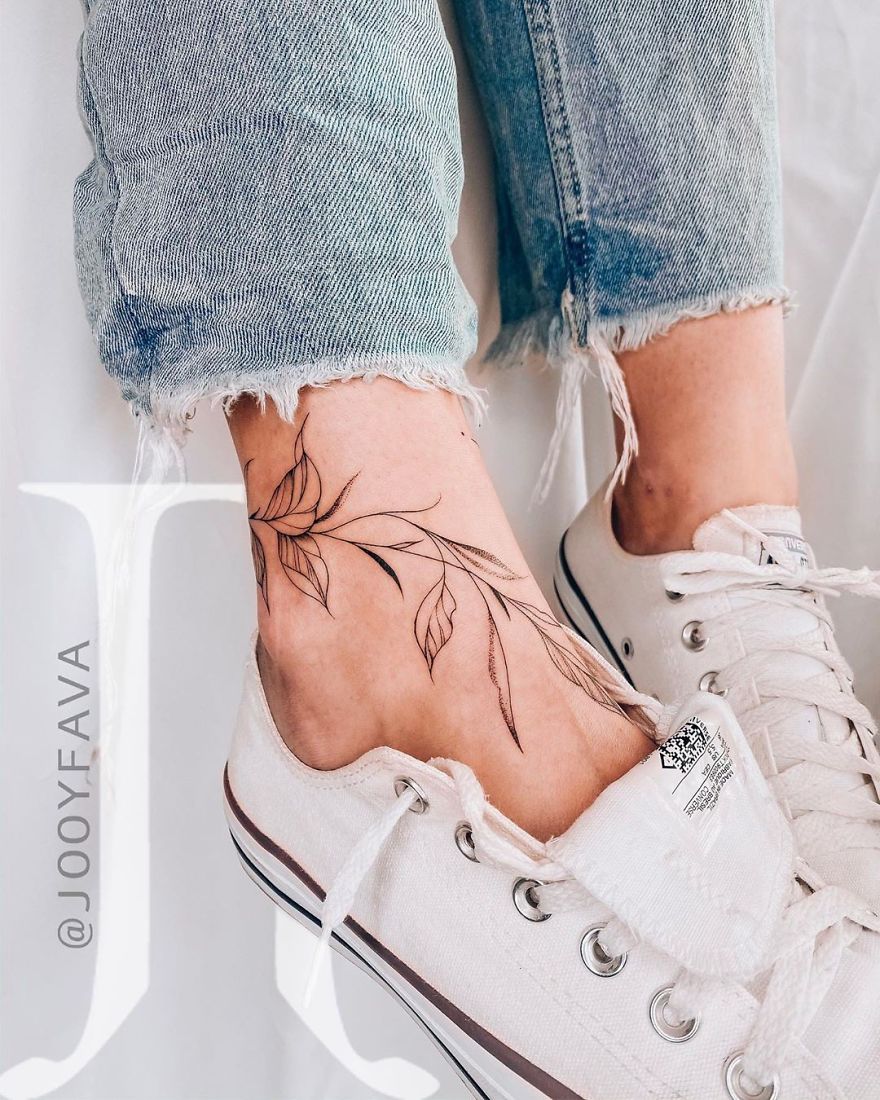 Delicate feminine tattoo of leaves on ankle, paired with frayed jeans and white sneakers.