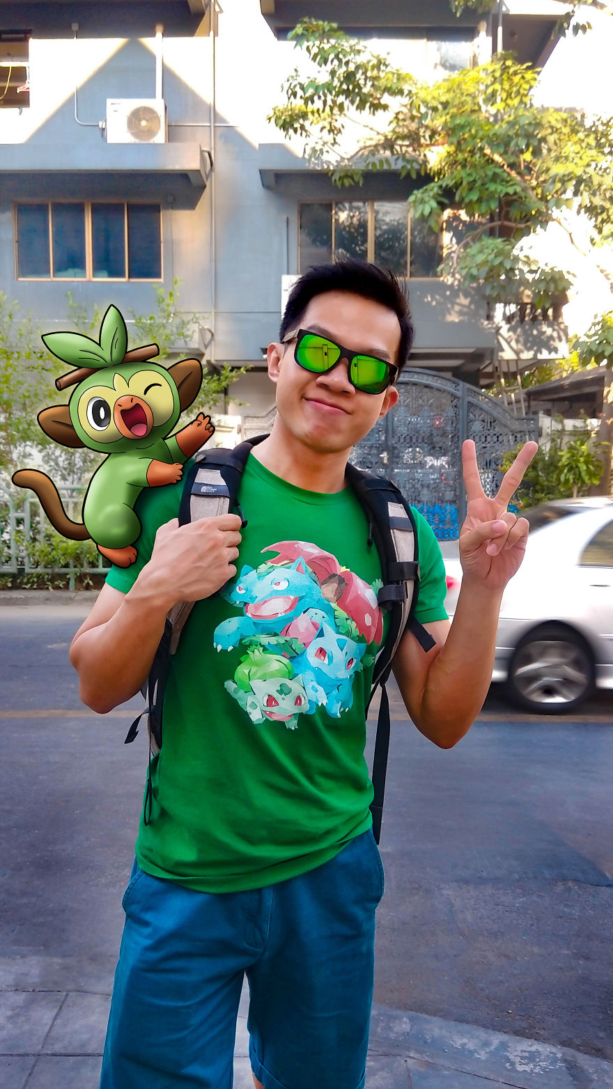 Man posing with Pokémon illustration on street, wearing green Pokémon shirt, showing peace sign.