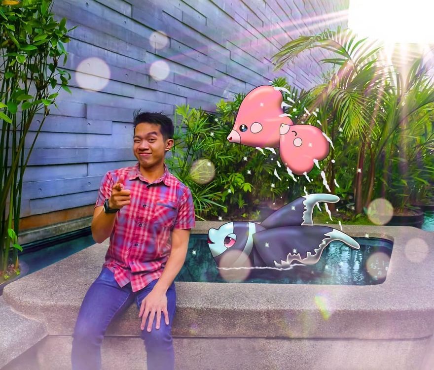 A person poses next to Pokémon illustrations by a pool, surrounded by lush greenery.
