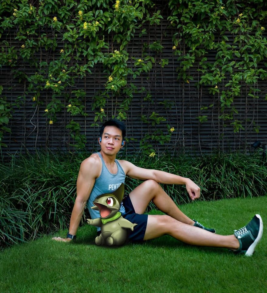 A man sitting on grass next to a Larvitar Pokémon illustration, surrounded by green foliage.